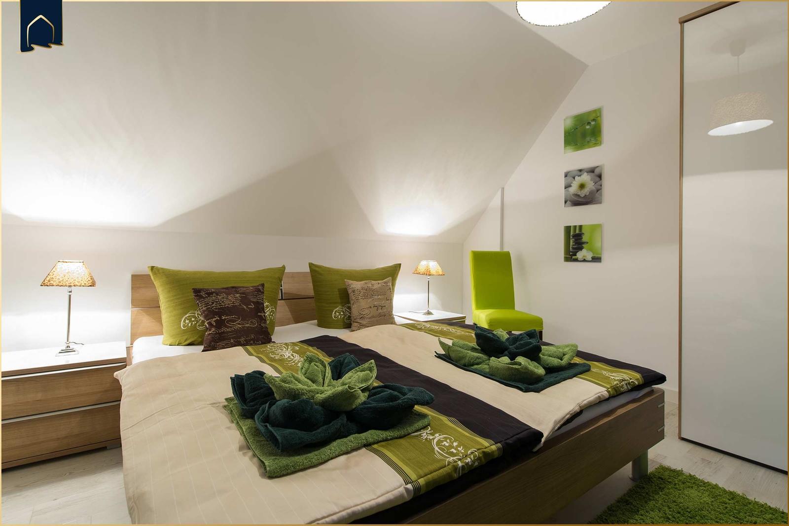 Schlafzimmer mit Dachschräge, Bett mit grünen Kissen und Handtuchblumen.