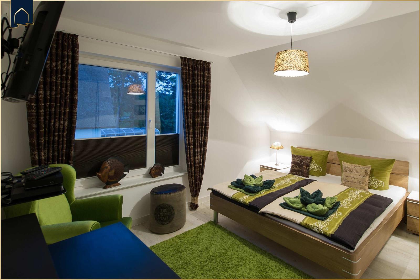 Schlafzimmer mit Bett, grünem Teppich und Fenster mit Vorhängen.