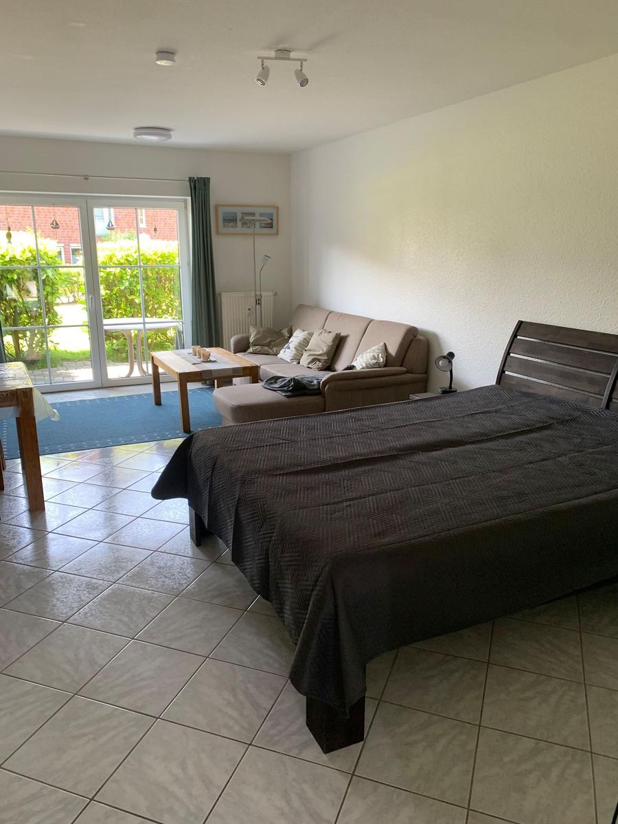 Schlafzimmer mit Sofa, Bett und Glastür zum Garten.
