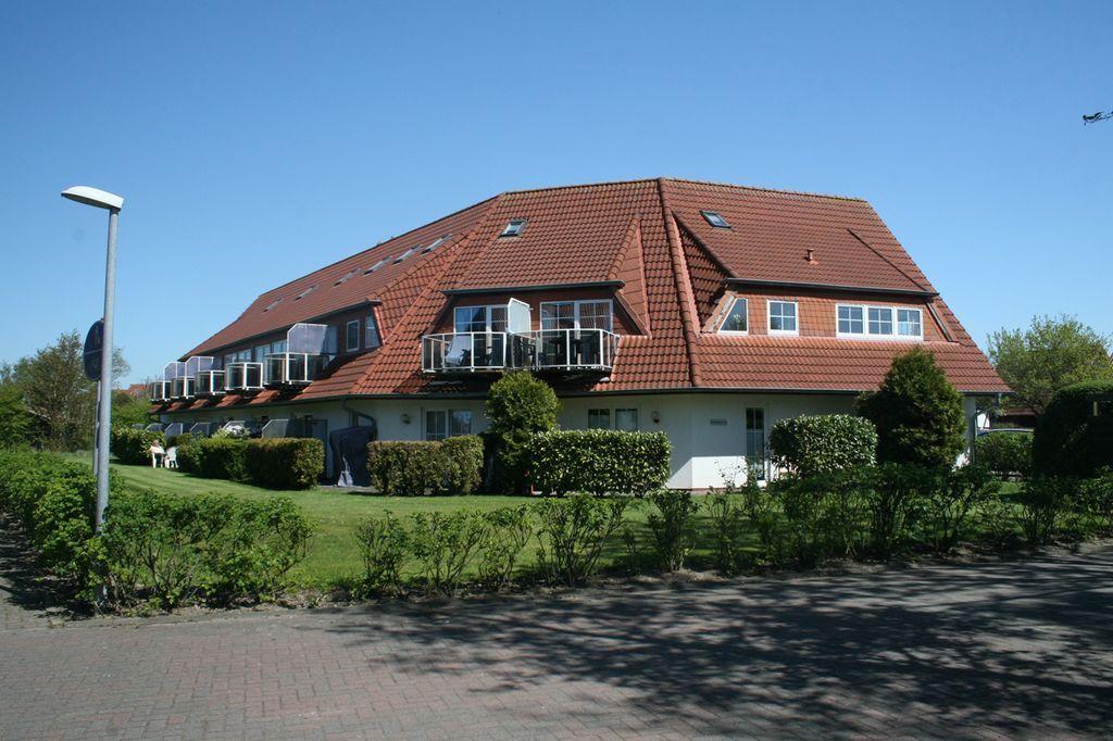 Modernes Mehrfamilienhaus mit Balkonen und rotem Dach unter blauem Himmel.