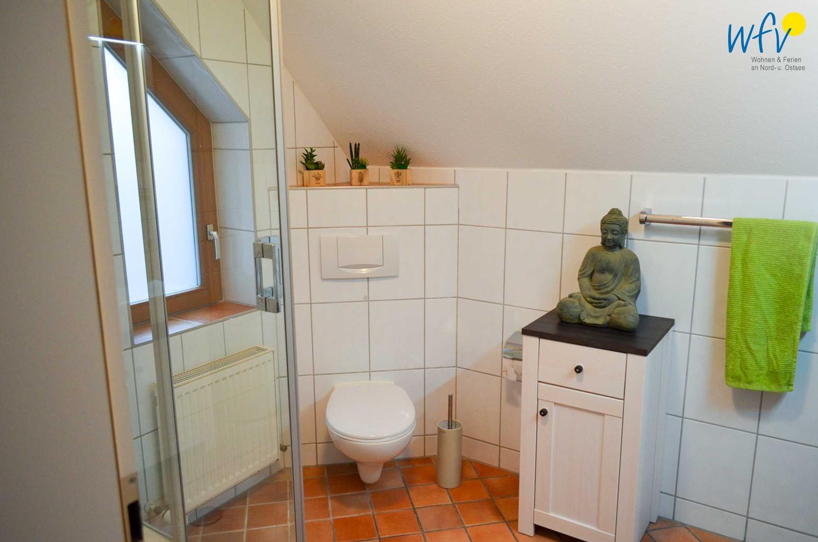 Badezimmer mit Dusche, Toilette und Buddha-Figur auf Schrank.