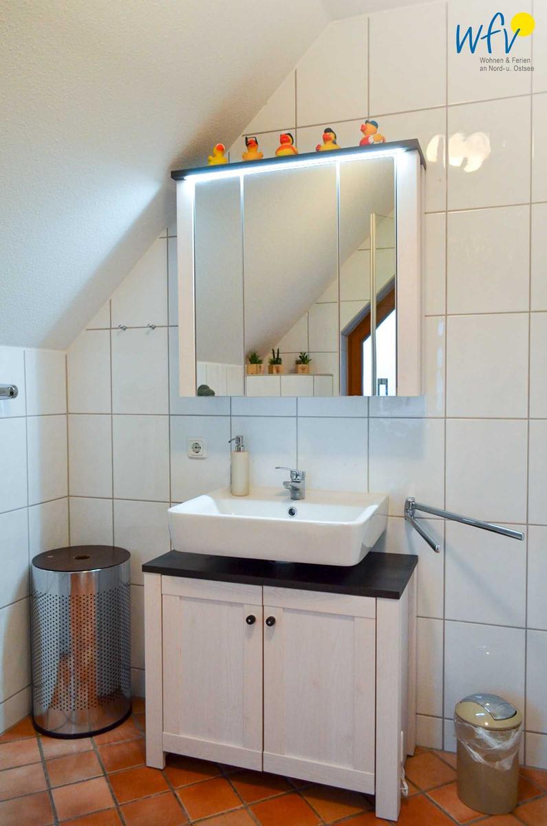 Badezimmer mit Waschbecken, Spiegelschrank und Duschbereich unter Dachschräge.