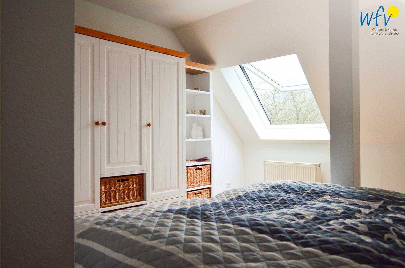 Schlafzimmer mit Dachfenster, weißem Schrank und gefüttertem Bett.