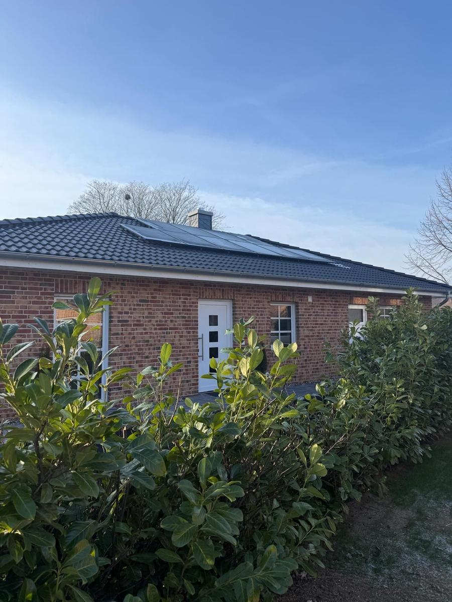 Ein Einfamilienhaus mit rotem Backstein und dunklem Dach unter blauem Himmel.