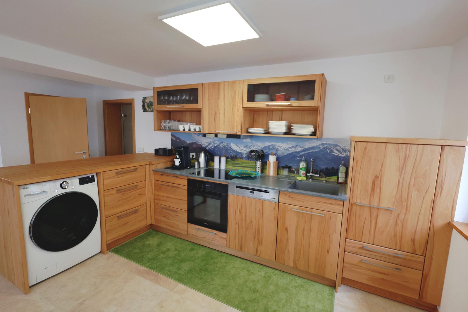 Küche mit Holzmöbeln, Spüle, Kochfeld und Waschmaschine.