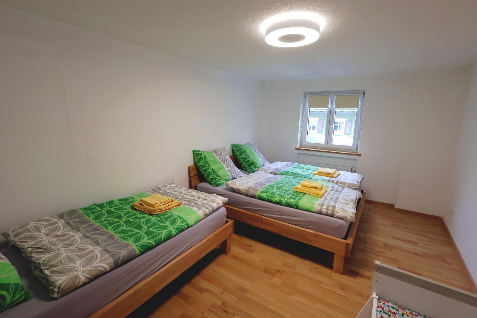 Zimmer mit zwei Betten, Holzboden und Fenster. Bettwäsche grün-weiß gemustert.