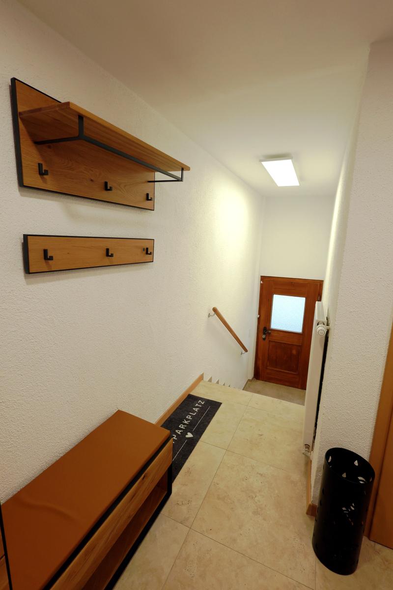 Eingangsbereich mit Holzregal, Bank und Tür mit Glasfenster.