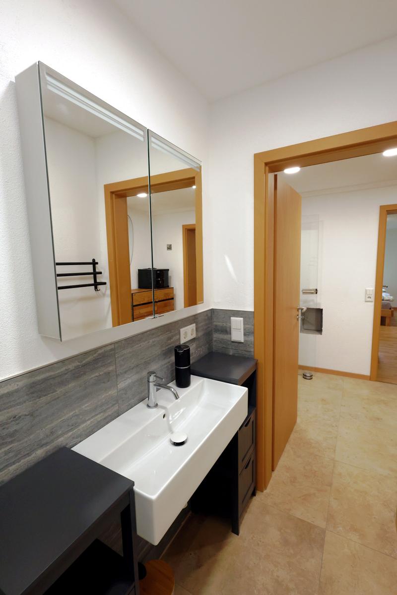 Badezimmer mit Waschbecken, Spiegelschrank und Tür zum Bad