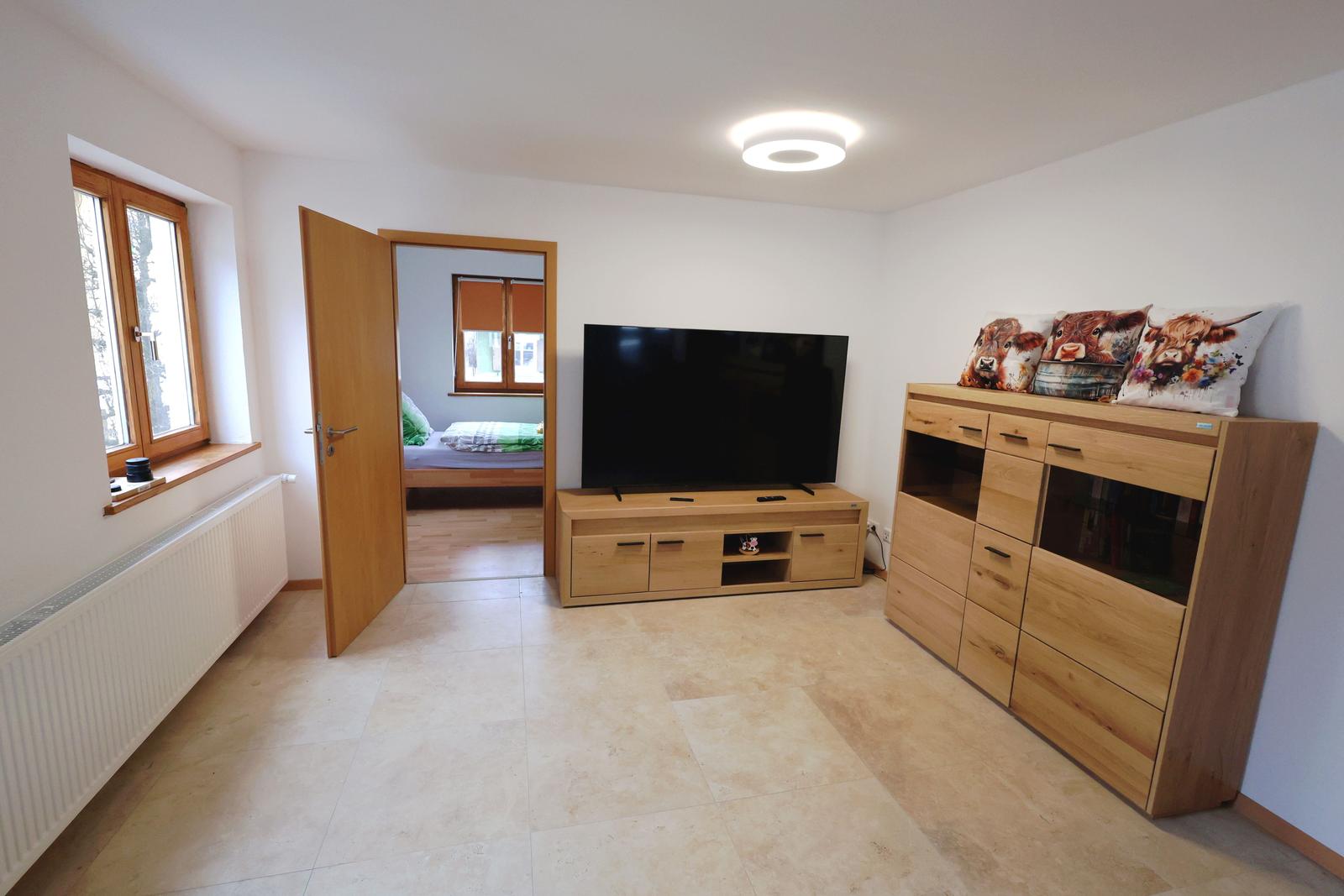 Wohnzimmer mit Fernseher, Holzmöbeln und Blick in Schlafzimmer.