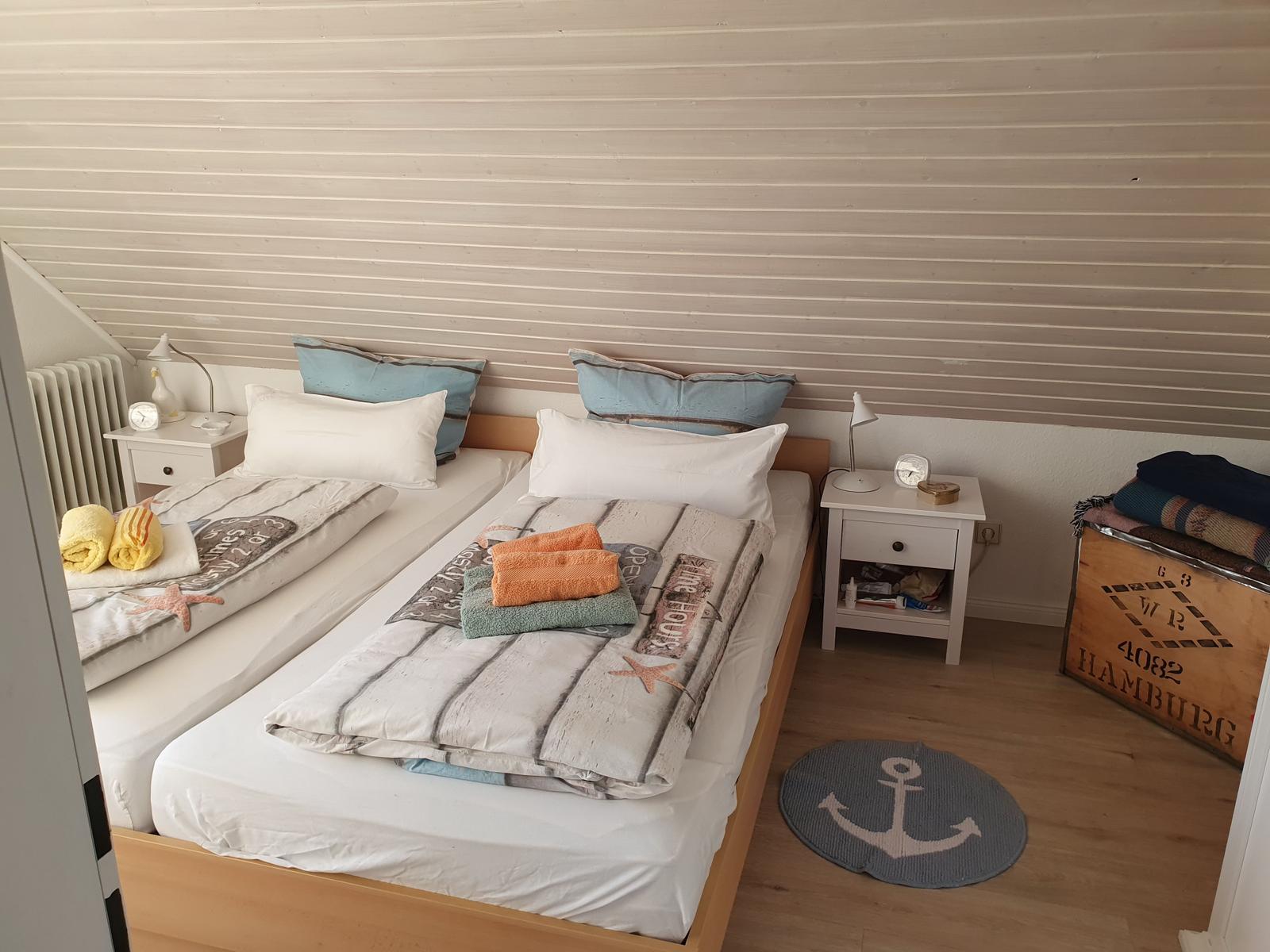 Zwei Betten mit Bettwäsche, Nachttische und Kisten im Schlafzimmer.