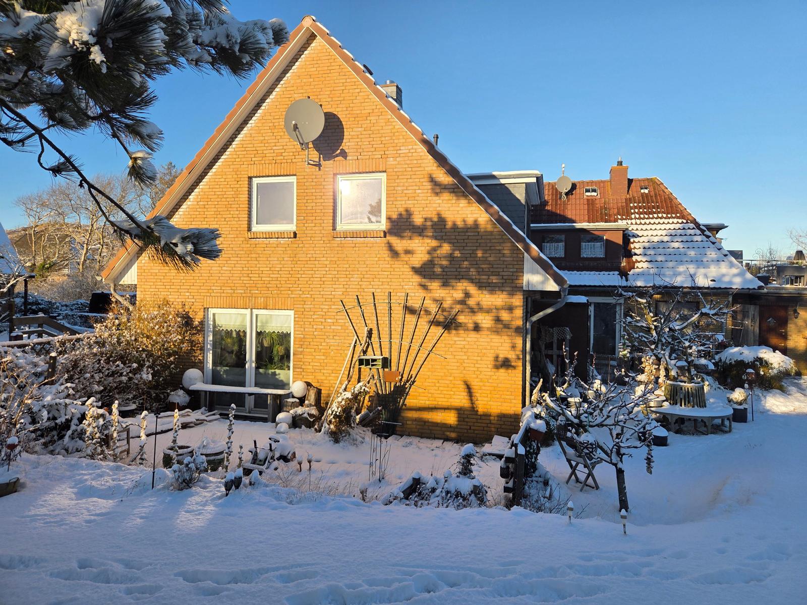 Ein zweistöckiges Haus mit Schnee bedecktem Garten und Satellitenschüssel.