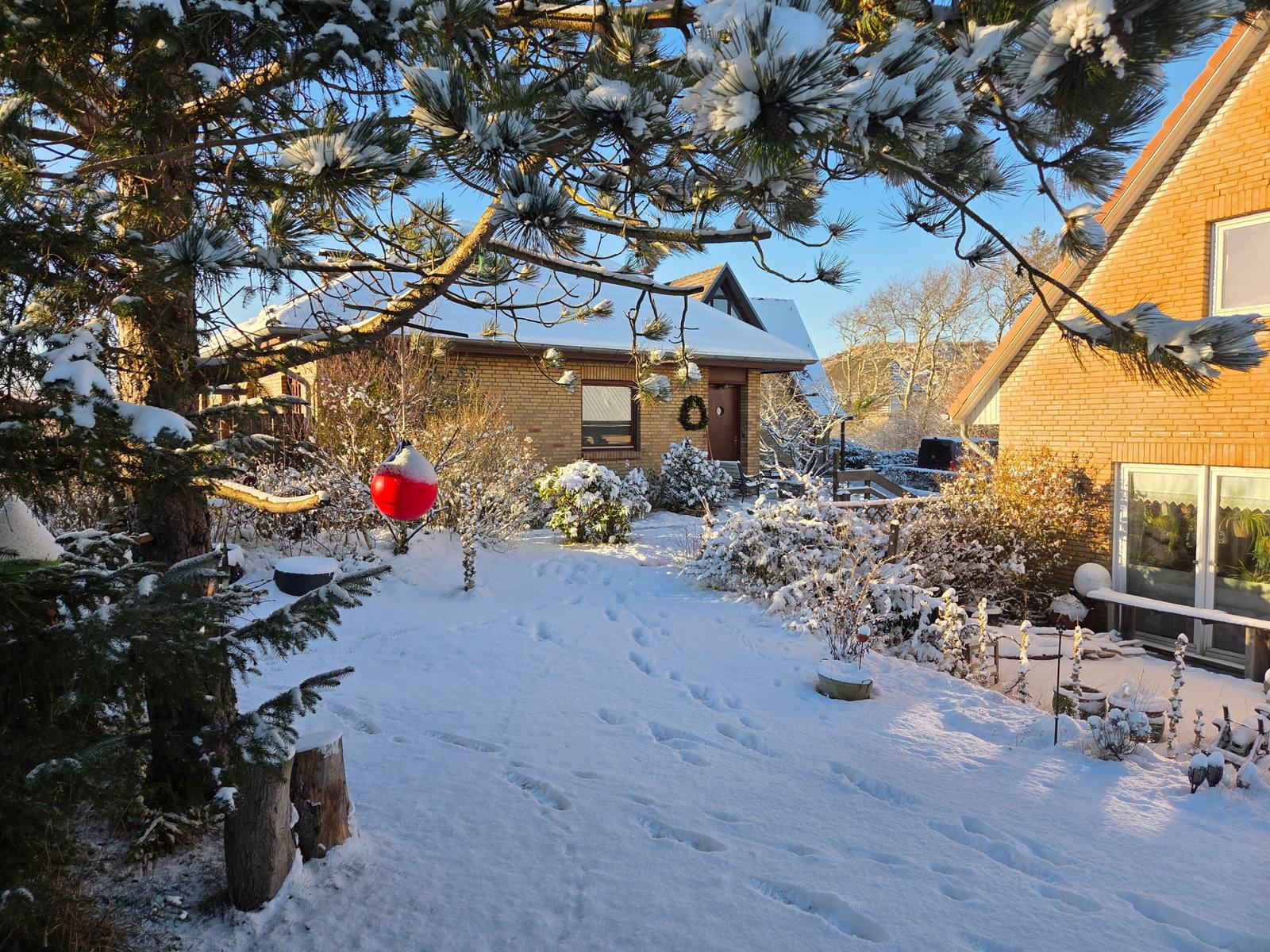 Schneebedeckter Garten mit rotem Weihnachtskugel und Haus im Hintergrund.