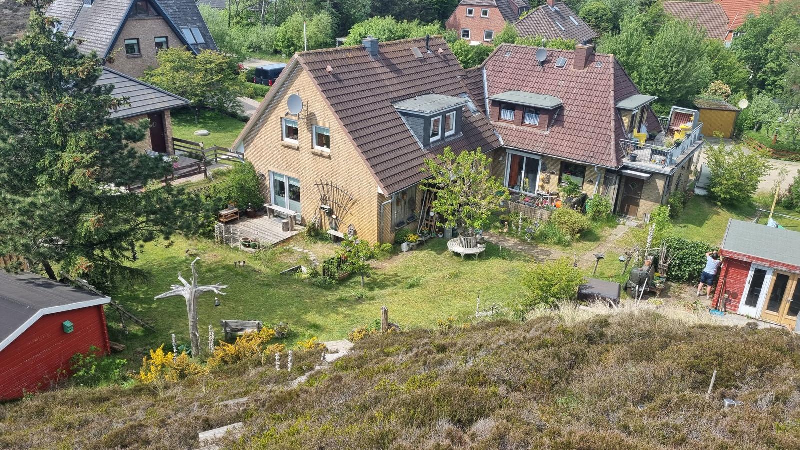 Haus mit Garten, Terrasse und kleinem Holzschuppen. Umgeben von Bäumen und Grünflächen.