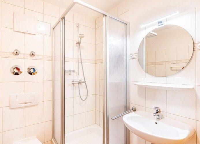 Badezimmer mit Dusche, Waschbecken und runden Spiegel.