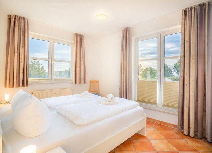 Schlafzimmer mit Doppelbett, zwei Fenstern und Terrasse.