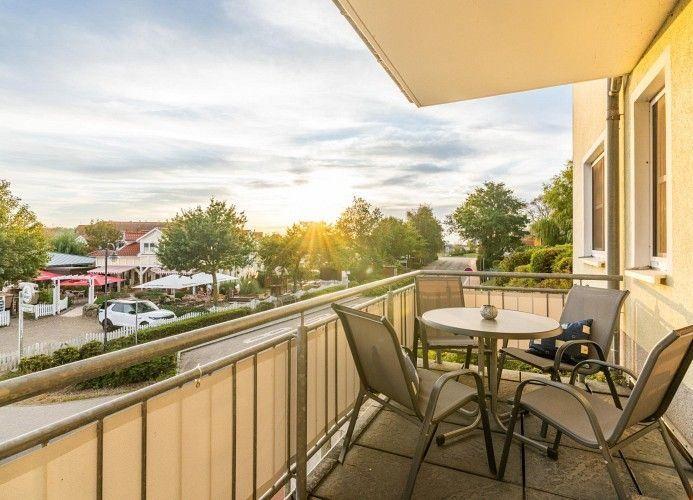 Terrasse mit Tisch und Stühlen. Blick auf Straße und Bäume bei Sonnenuntergang.