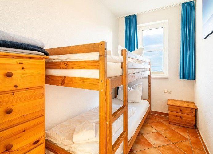 Zimmer mit Doppelstockbett, Holzschrank und Fenster mit Blick aufs Meer.