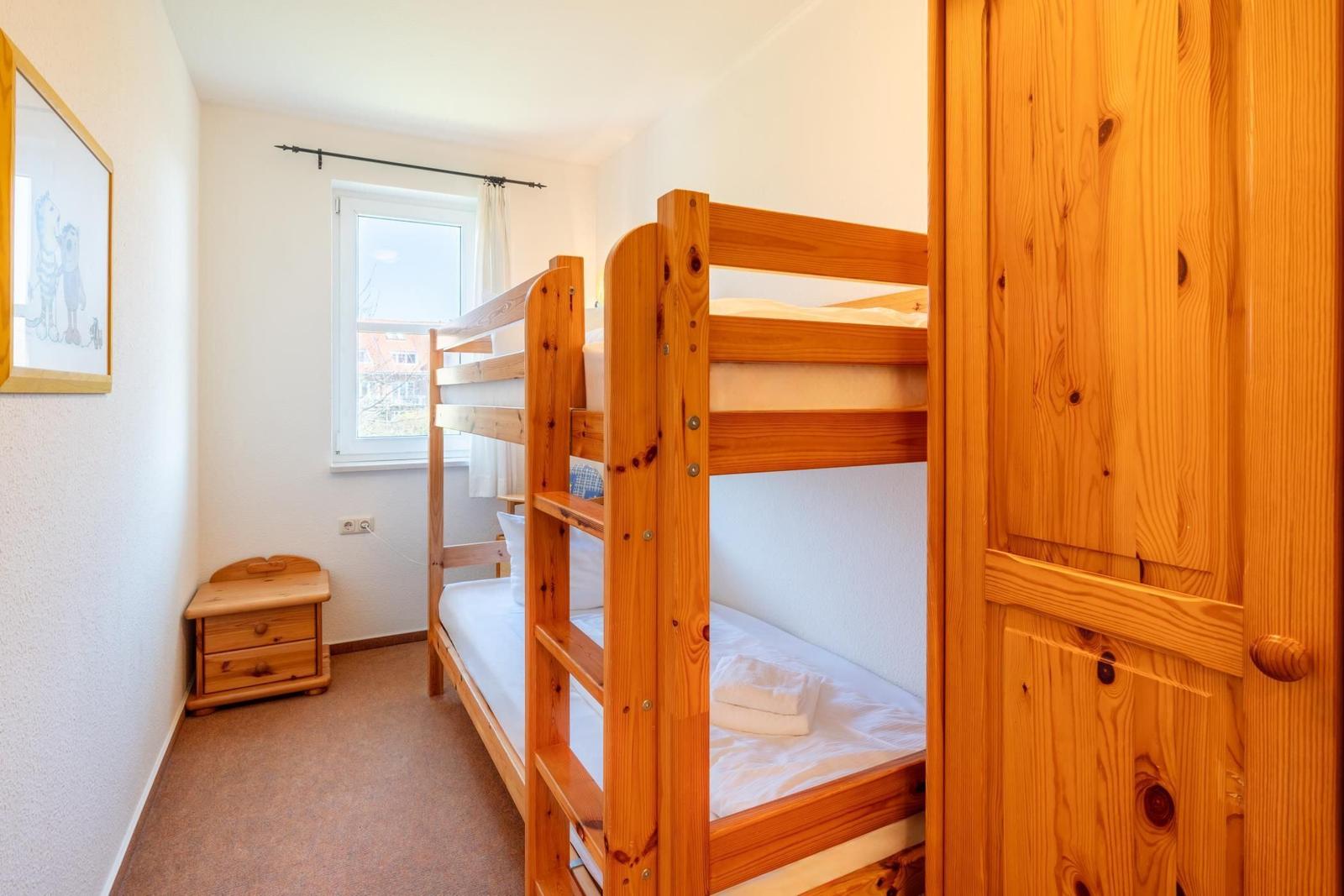 Ein Schlafzimmer mit Holz-Etagenbett, Kleiderschrank und Fenster.