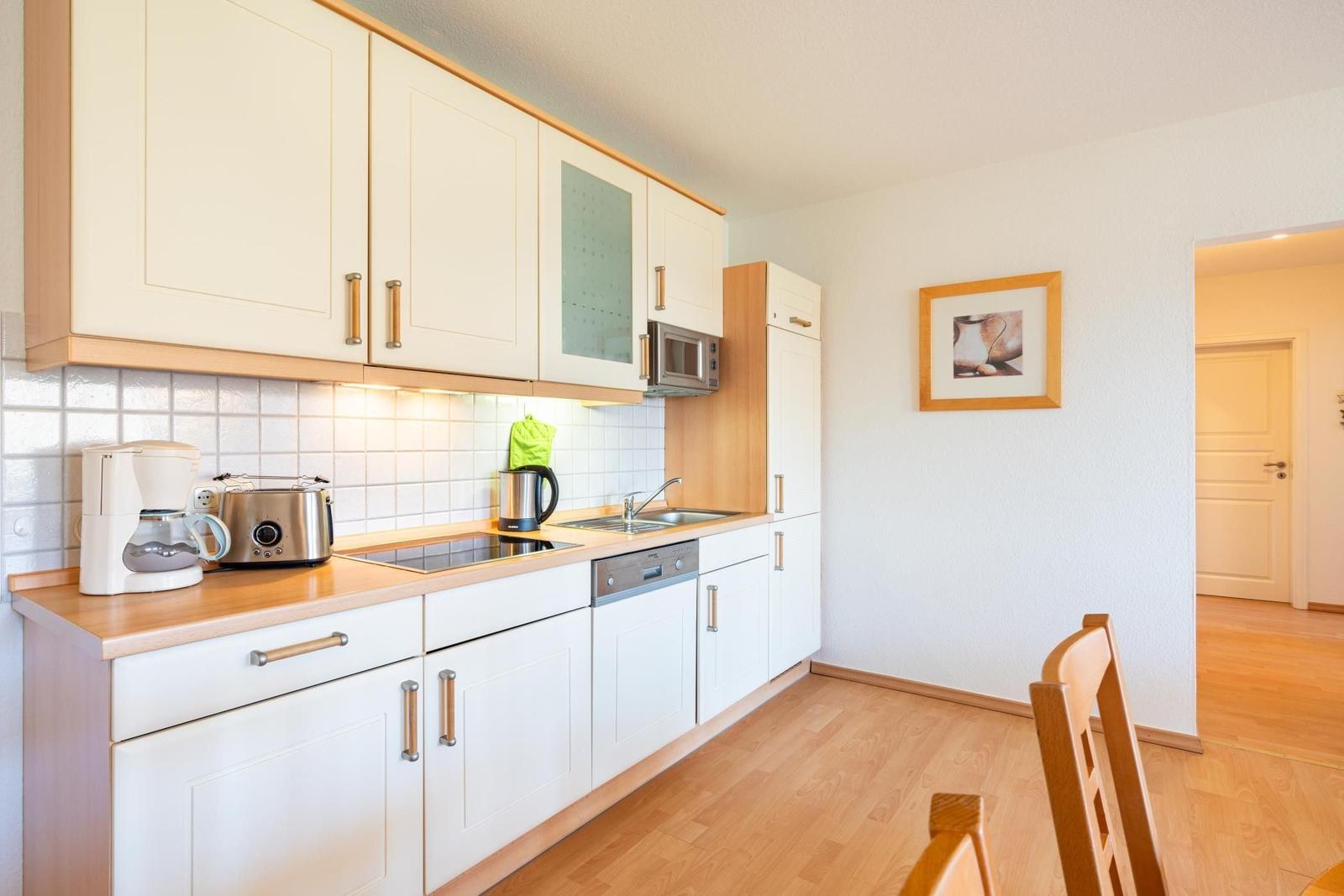 Küche mit weißen Schränken, Holzoberfläche und Küchengeräten.