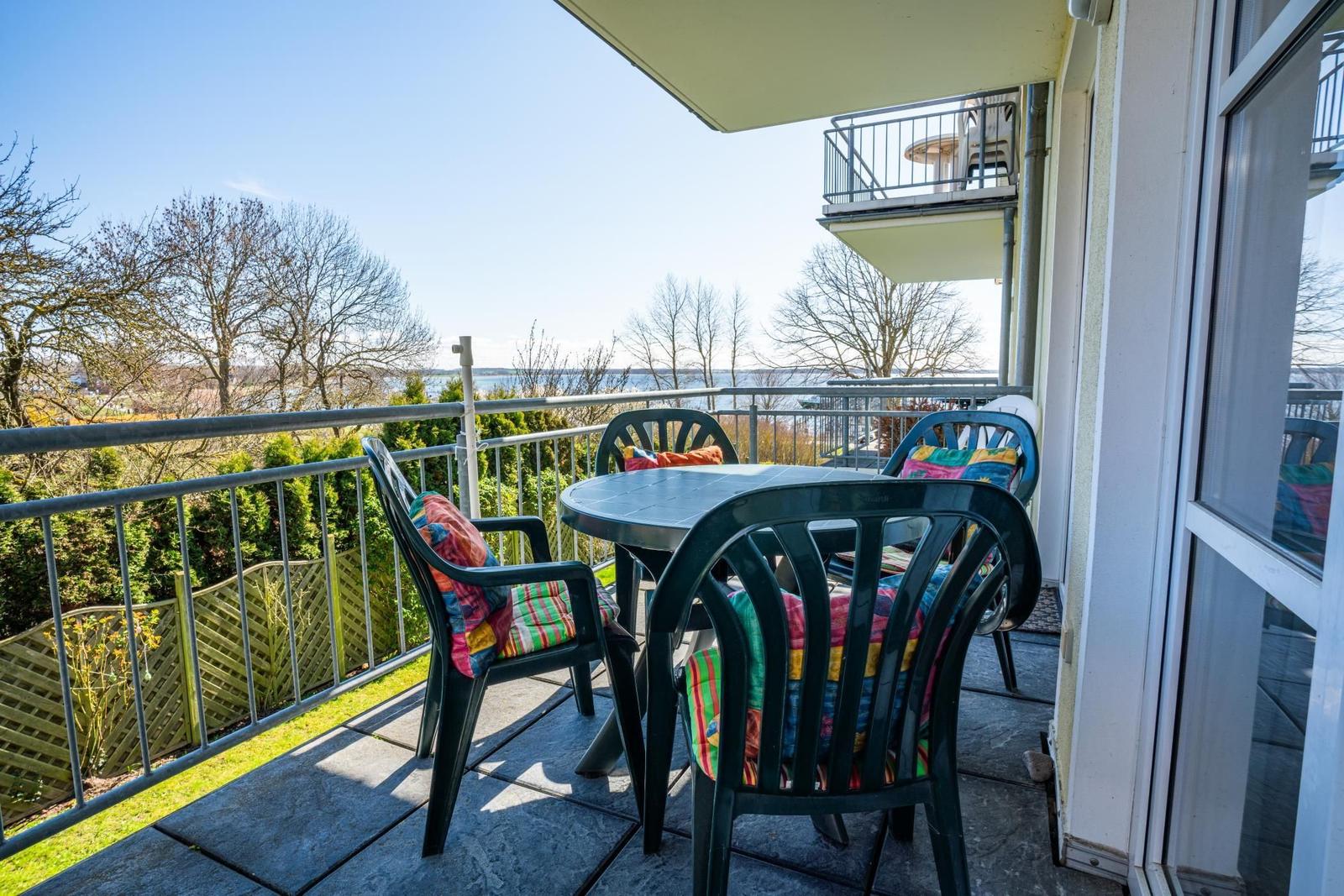Terrasse mit Tisch und Stühlen, Blick auf Wasser und Bäume.