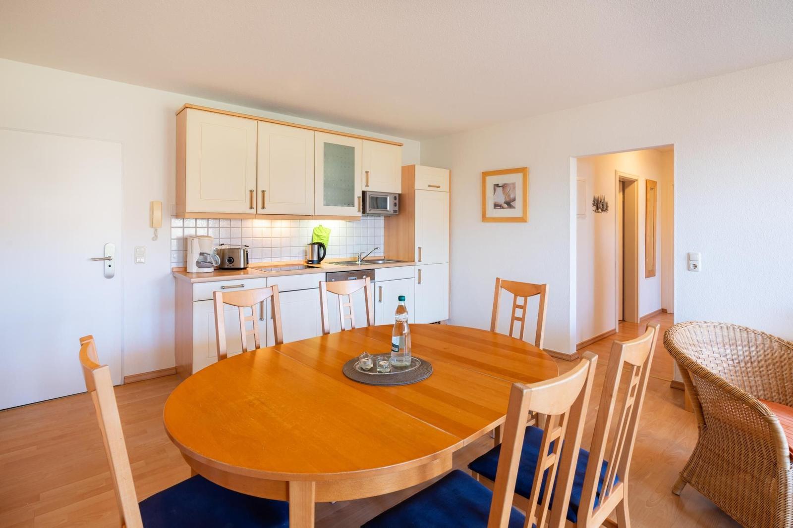 Essbereich mit runden Tisch und Stühlen, Küche mit weißen Schränken und Mikrowelle.