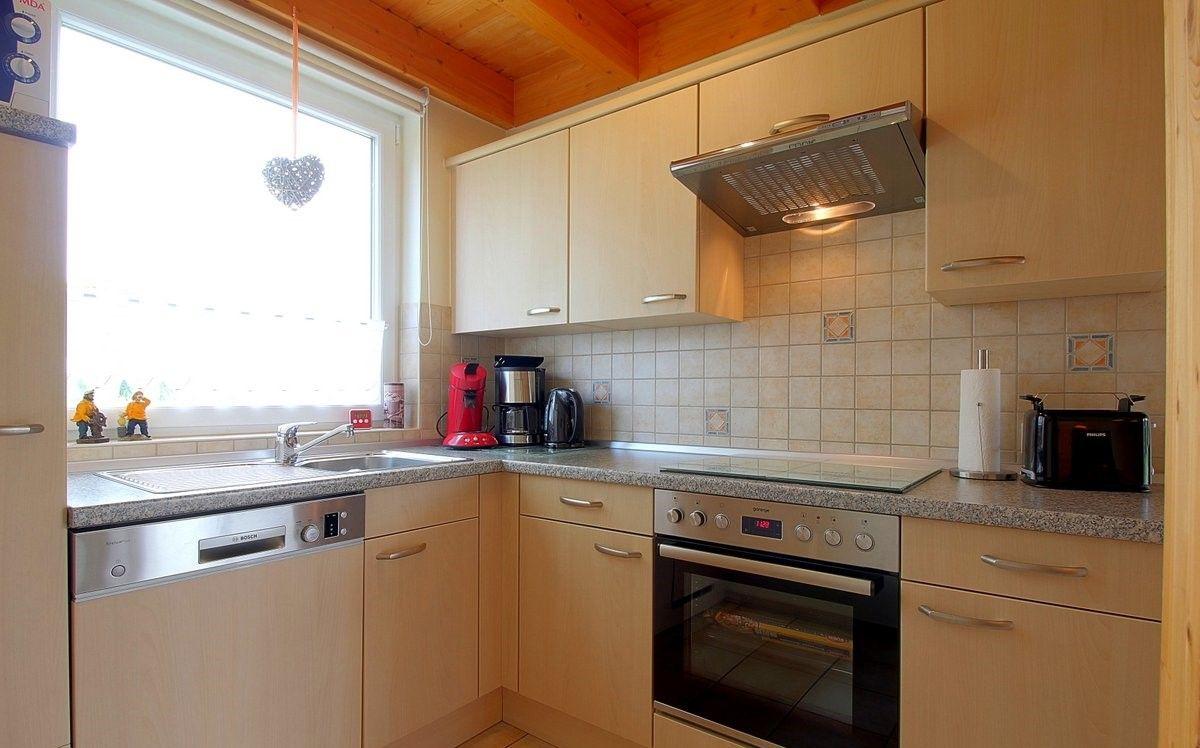 Küche mit Holzschränken, Spüle, Herd und Backofen. Fenster mit Herzschmuck.