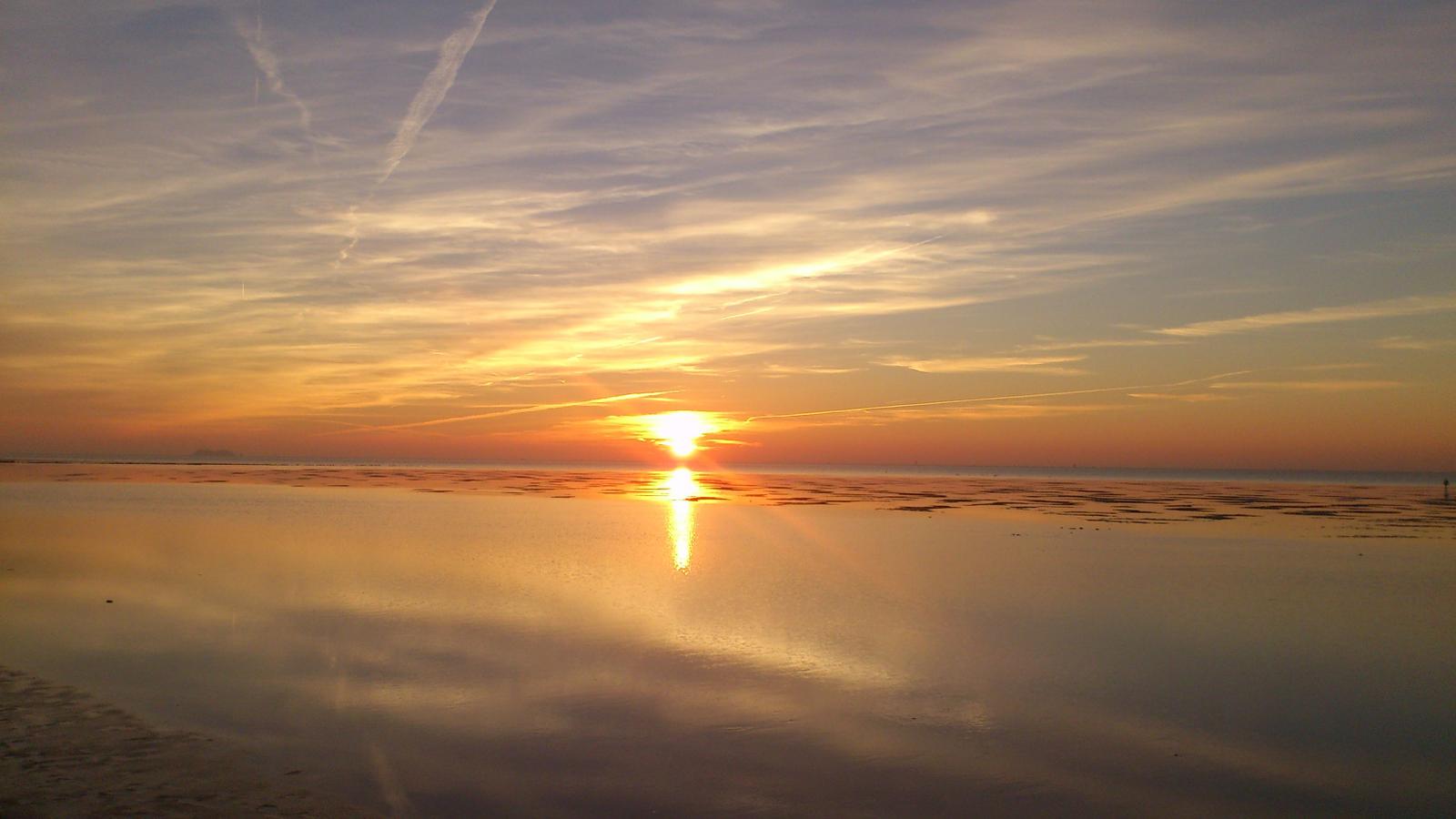 Sonnenuntergang über Flachwasser mit Reflexion und Wolken.