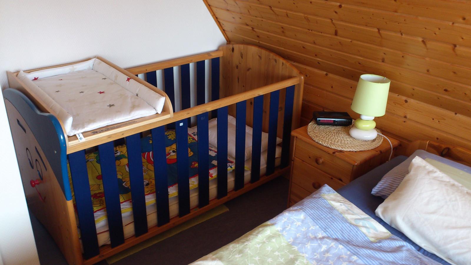 Kinderbett mit Wickelplatz und Nachttisch mit Lampe und Wecker.