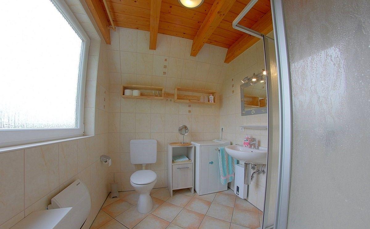 Badezimmer mit Dusche, Waschbecken, Toilette und Holzdecke.