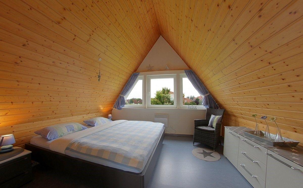 Schlafzimmer mit Holzwand und Dachfenster. Bett, Sessel und Schrank sind vorhanden.