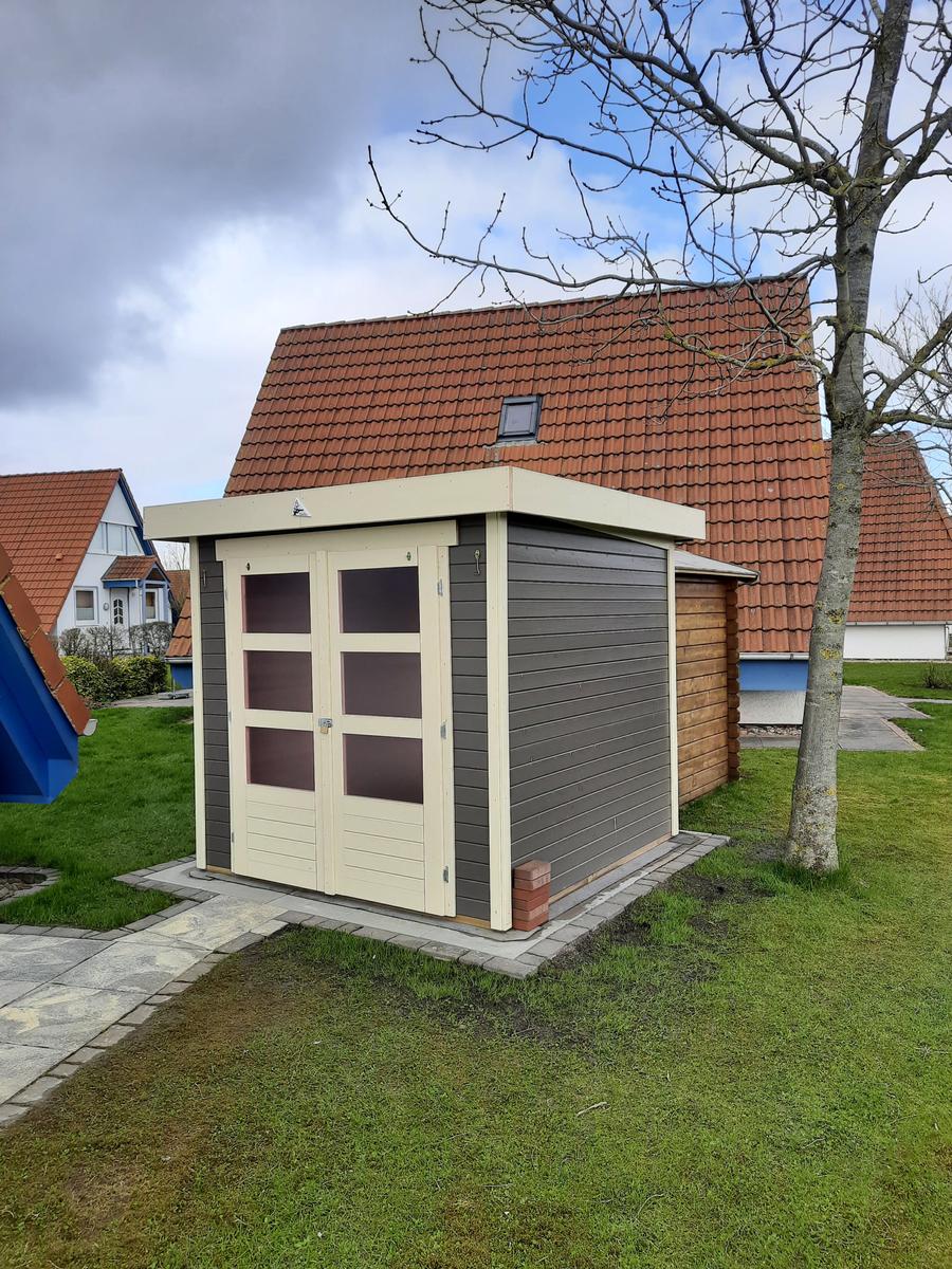 Holzgarage mit Doppeltür und Dachfenster im Garten.