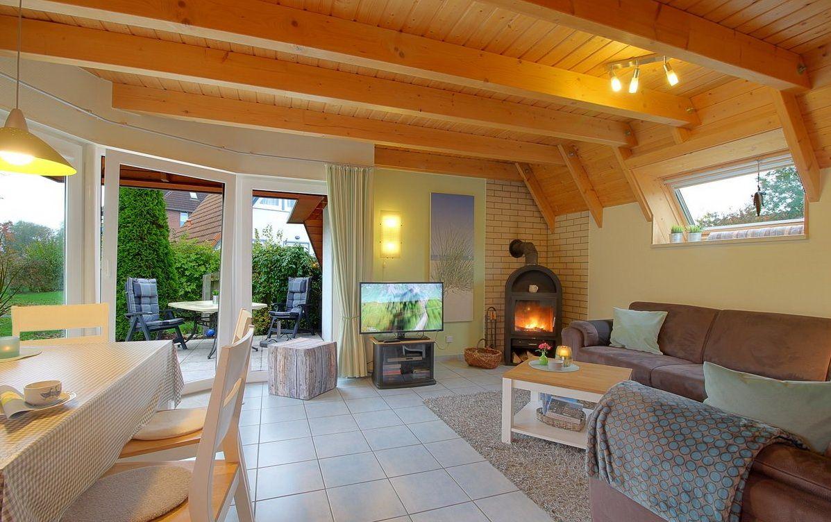 Wohn- und Essbereich mit Holzdecke, Kamin und Blick auf den Garten.