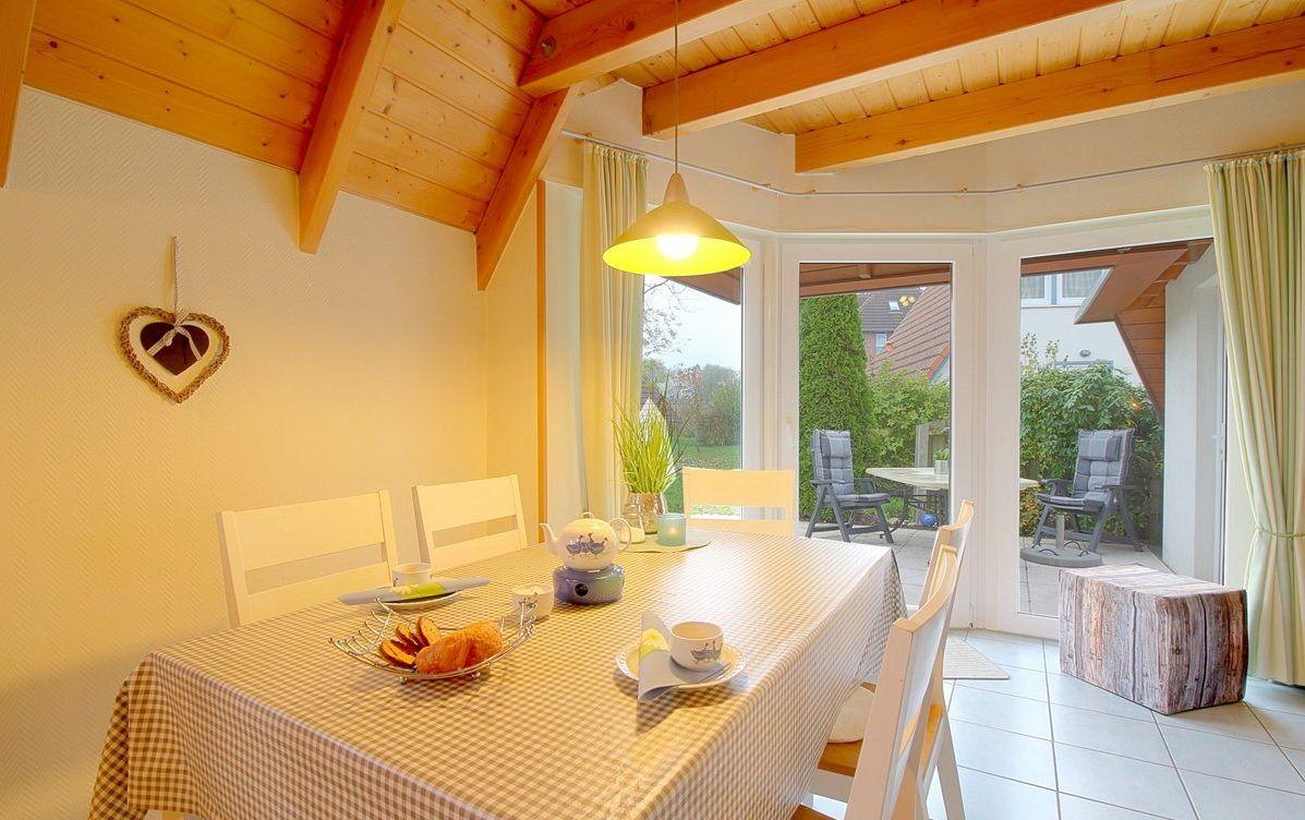 Esszimmer mit Holzdecke, Tisch mit Tischdecke und Blick auf Terrasse.