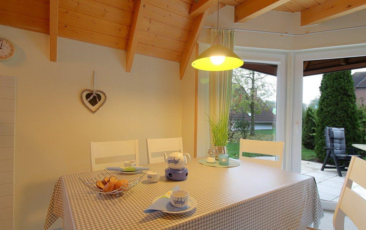 Esstisch mit Tischdecke und Stühlen unter Holzdecke mit Blick auf Garten.