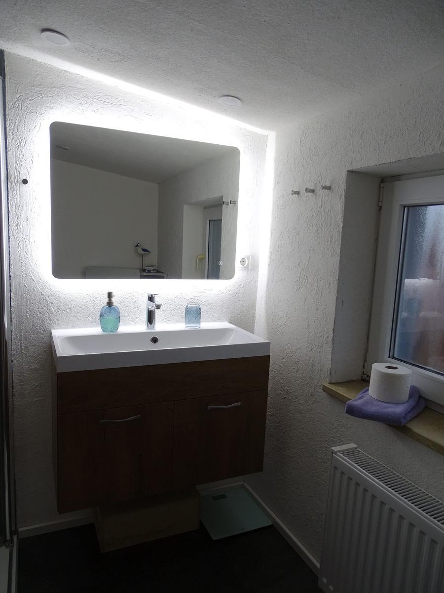 Bad mit beleuchtetem Spiegel, Waschbecken und Fenster.