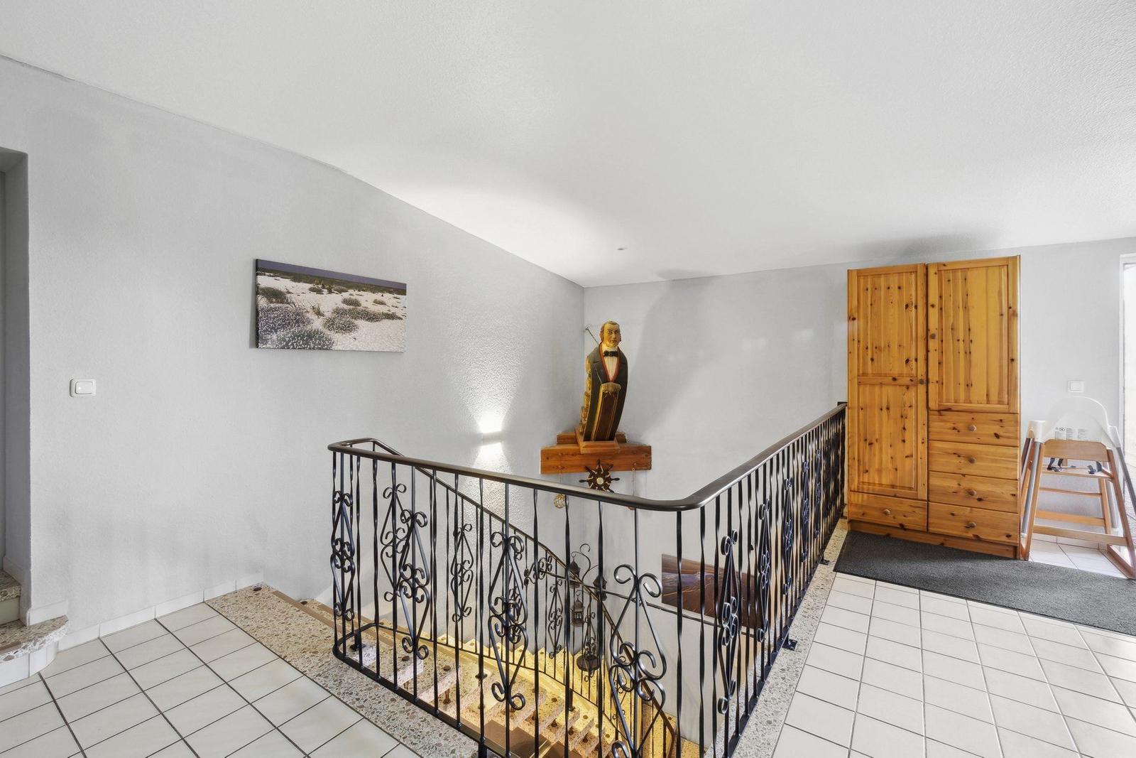 Eingangsbereich mit Treppe, Holzschrank und Skulptur an der Wand.