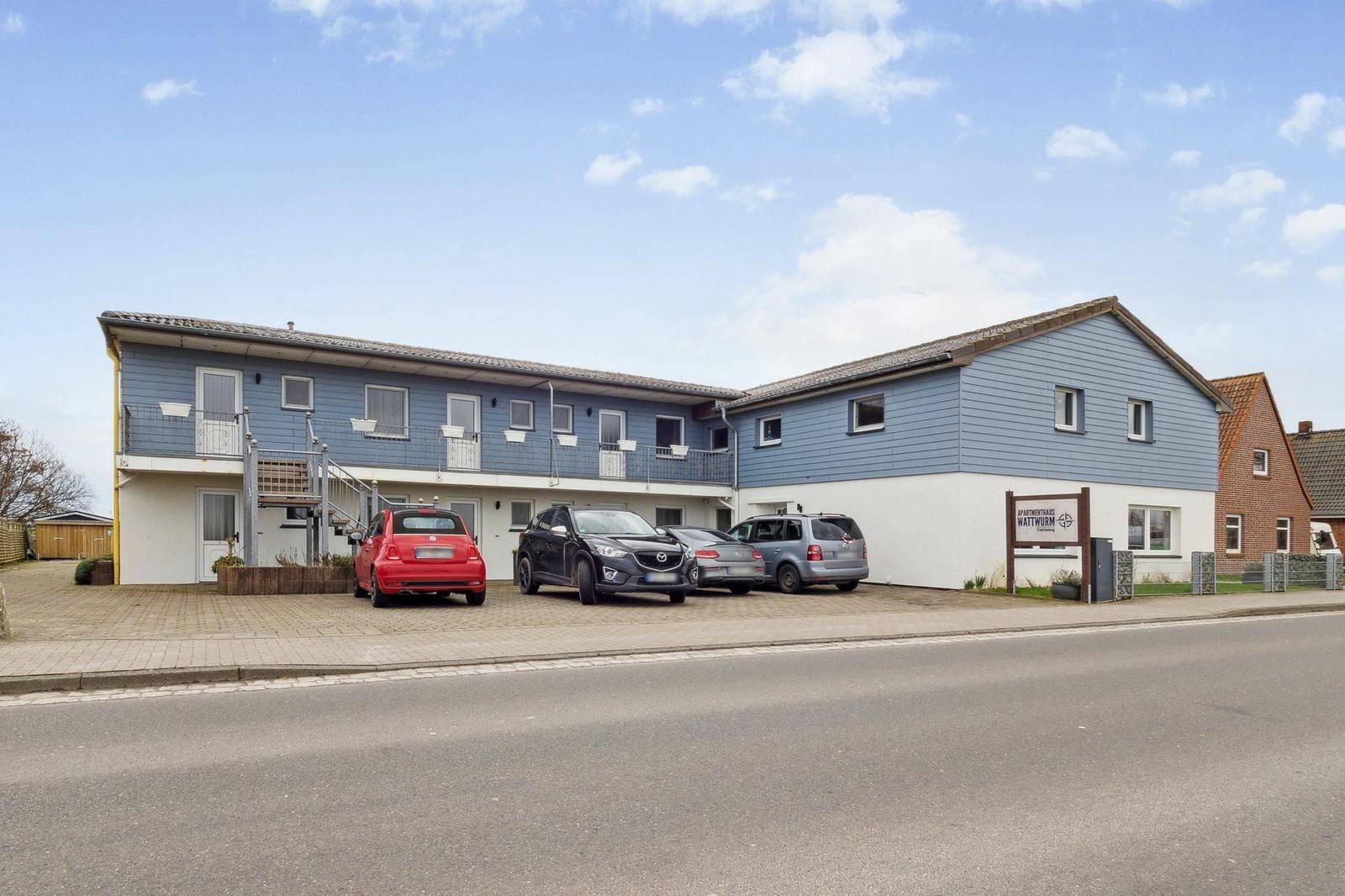 Apartmenthaus mit Balkonen und Parkplatz vorne.