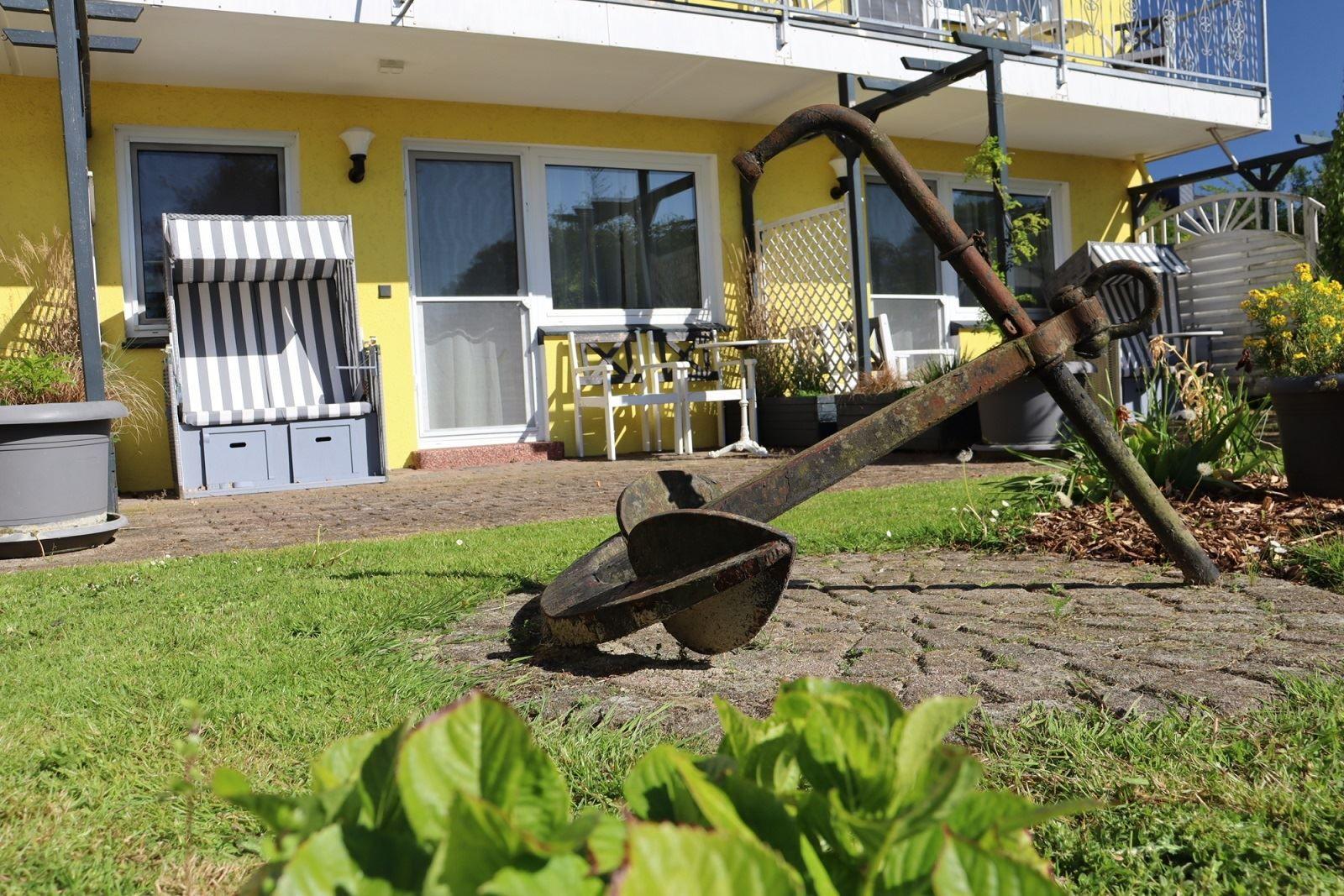 Vor dem Haus steht ein großer, rostiger Anker auf dem Rasen.