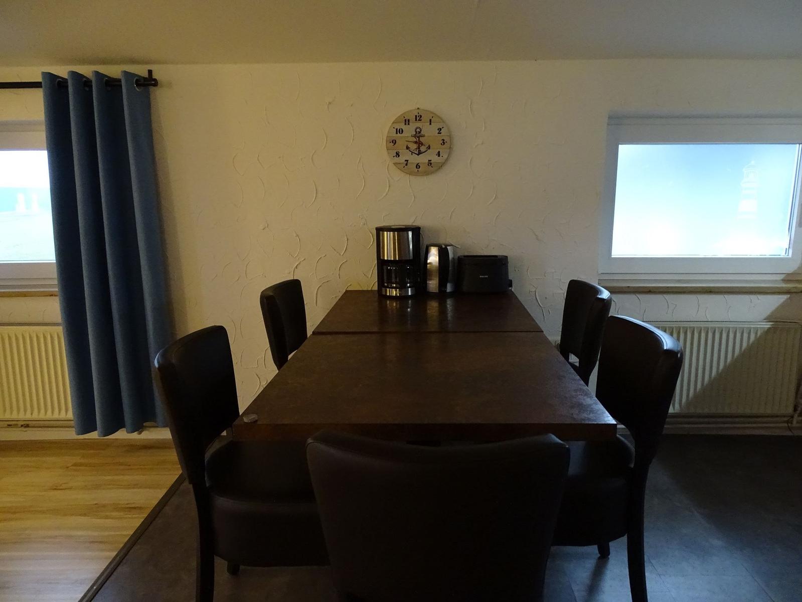 Esstisch mit sechs Stühlen, Wanduhr und Fenster mit Blick auf Leuchtturm.