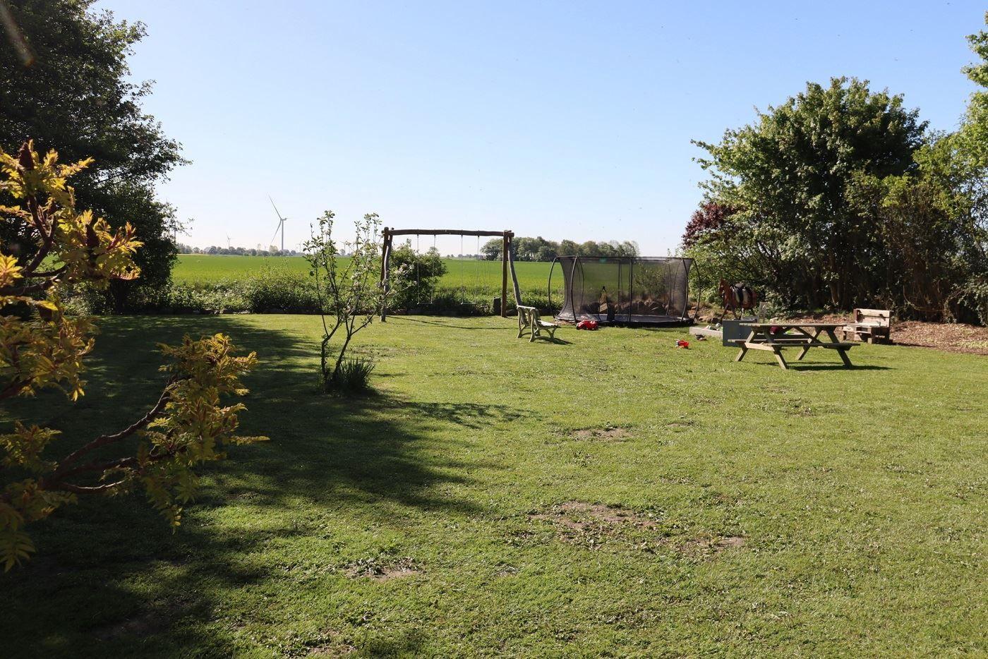 Großer Garten mit Schaukel, Trampolin und Picknicktisch. Blick auf grüne Felder und Windkraftanlage.