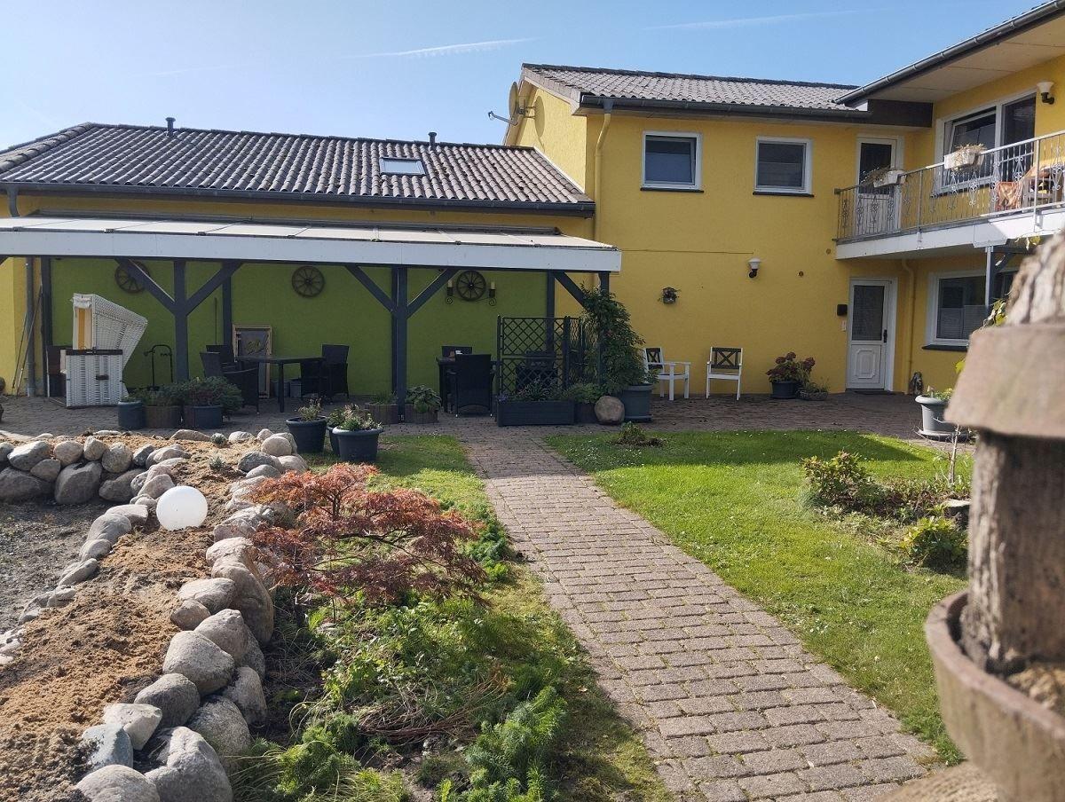 Haus mit gelber Fassade, Gartenbereich und gepflastertem Weg.