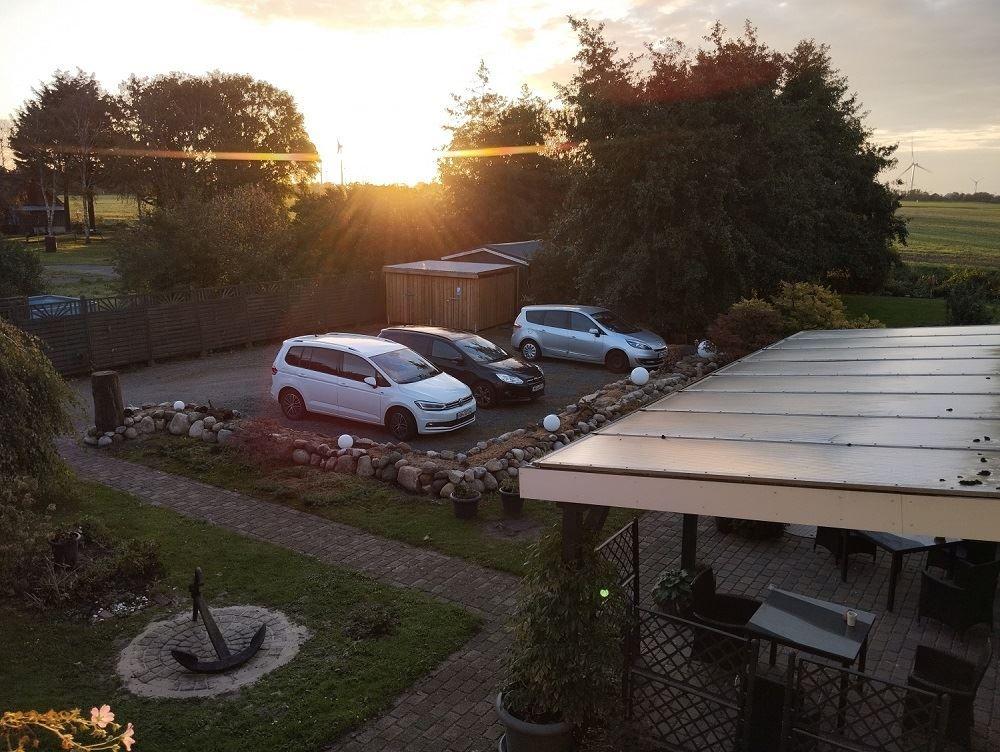 Parkplatz mit drei Autos, Terrasse und Garten bei Sonnenuntergang.