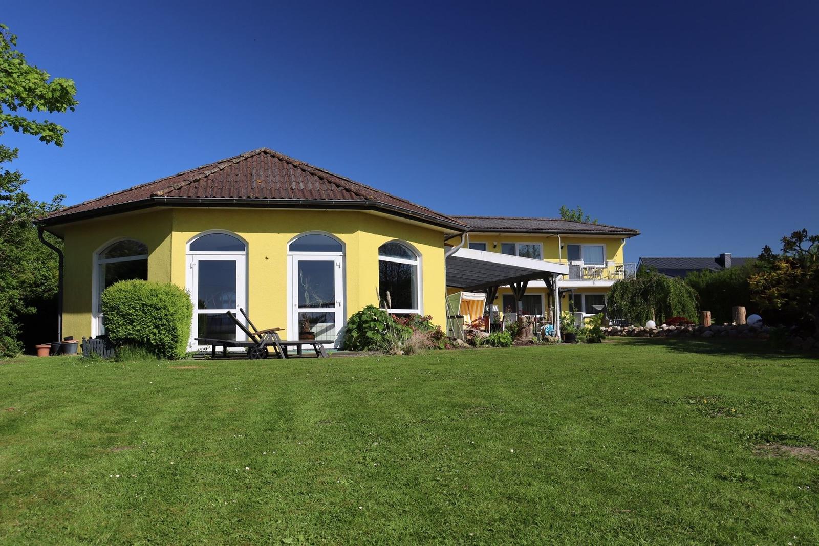 Gelbes Haus mit Terrasse und grünem Garten unter blauem Himmel.