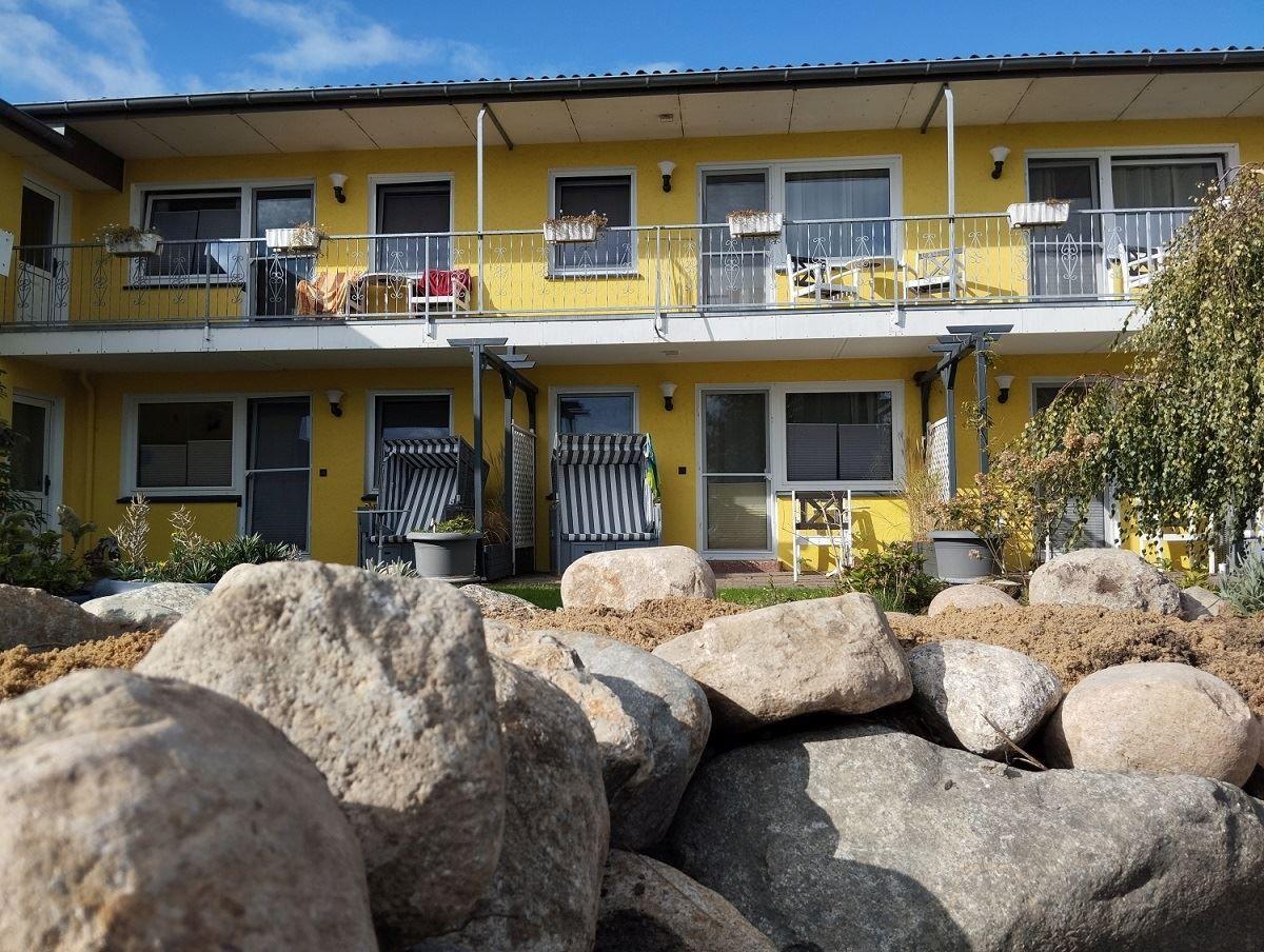 Gelbes Mehrfamilienhaus mit Balkonen und Garten. Große Steine im Vordergrund.