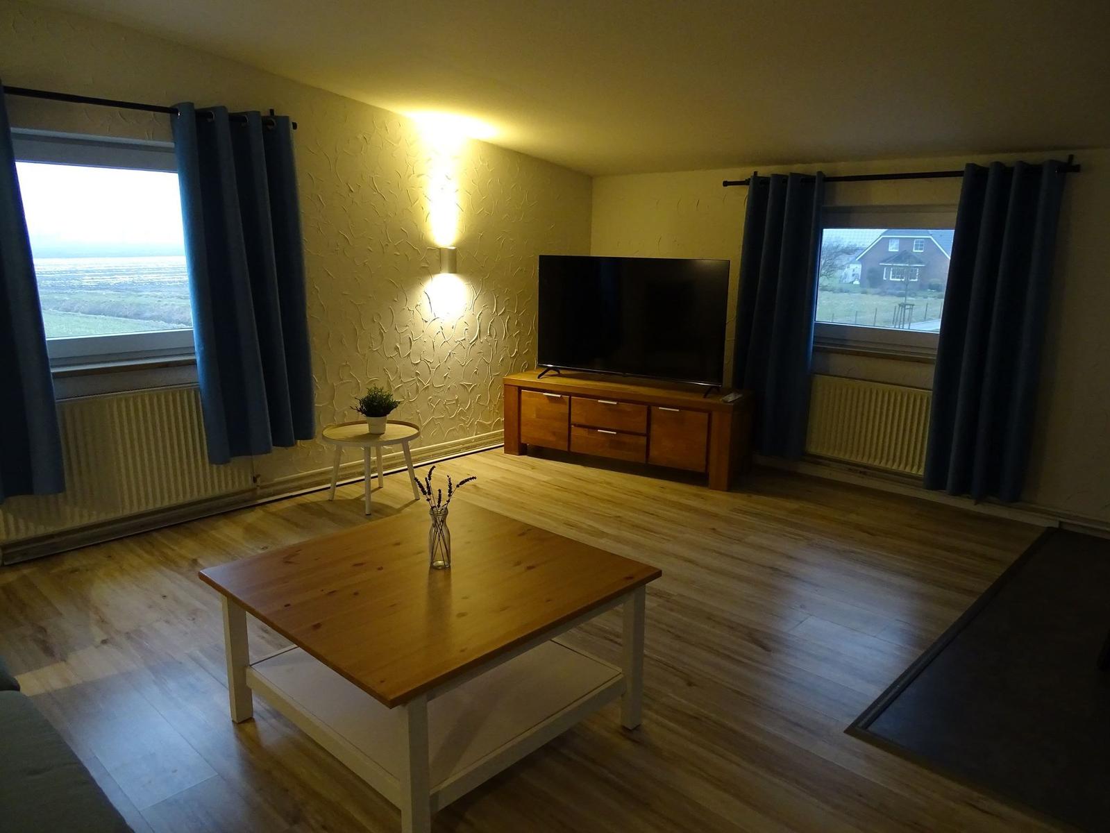 Wohnzimmer mit Holzboden, TV, Tisch und Fenstern mit Blick.