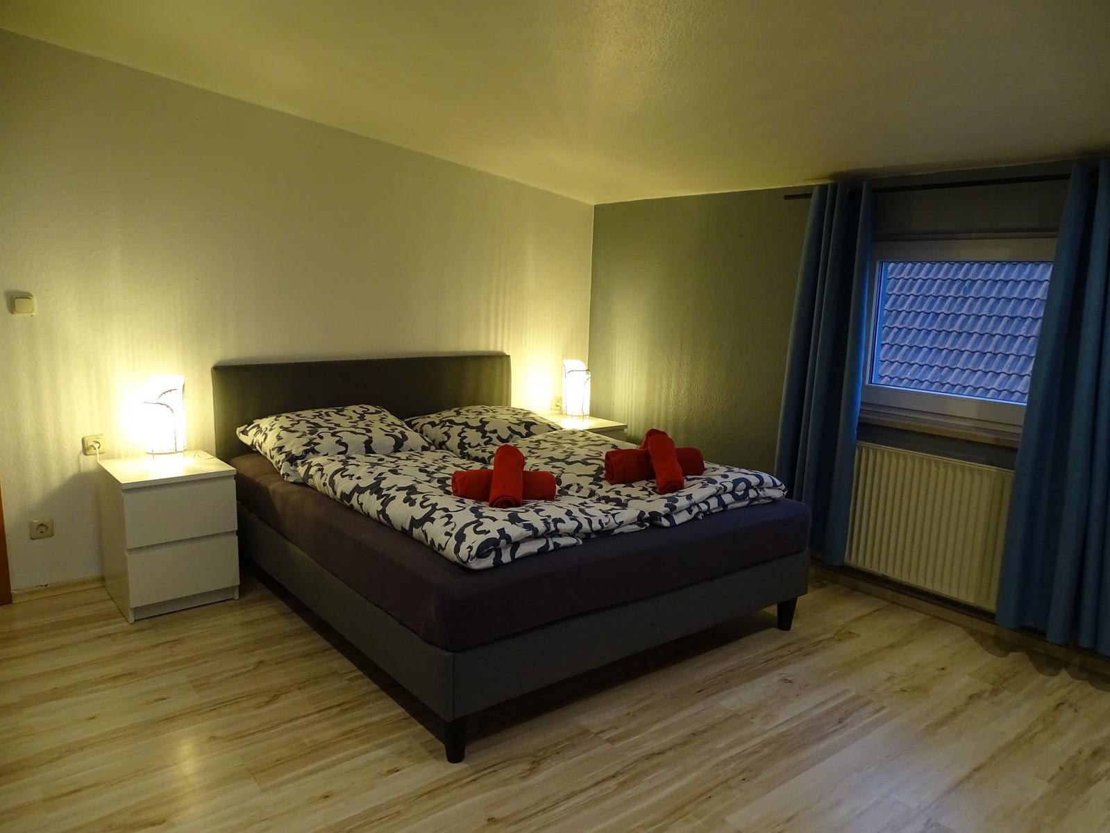 Schlafzimmer mit Doppelbett, zwei Nachttischen und Fenster mit Vorhängen.