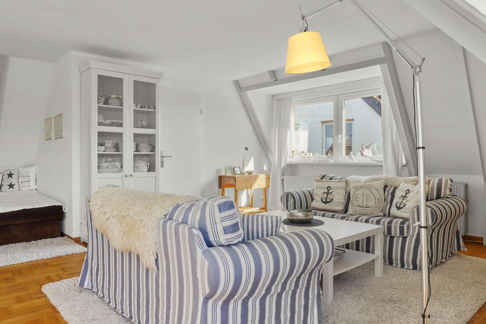 Wohnzimmer mit gestreiftem Sofa, Glaswand-Schrank und Fenster mit Blick.