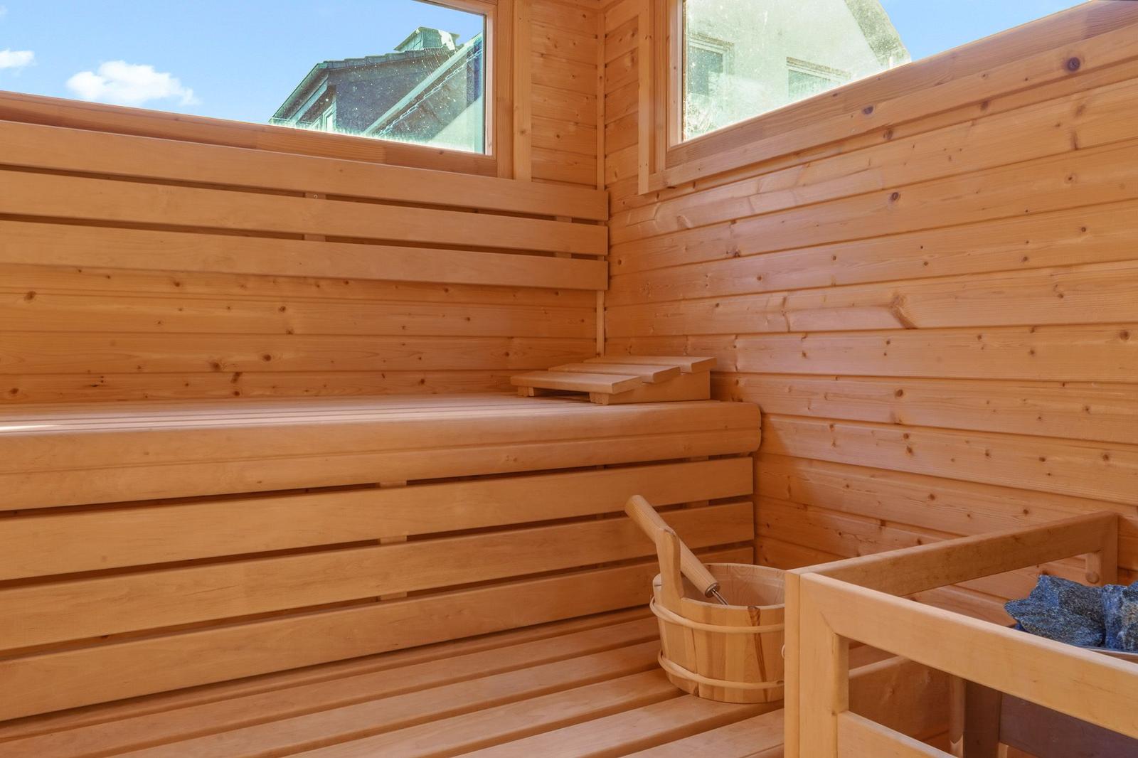 Holzsauna mit Sitzbänken und Eimer. Fenster bieten Blick nach draußen.