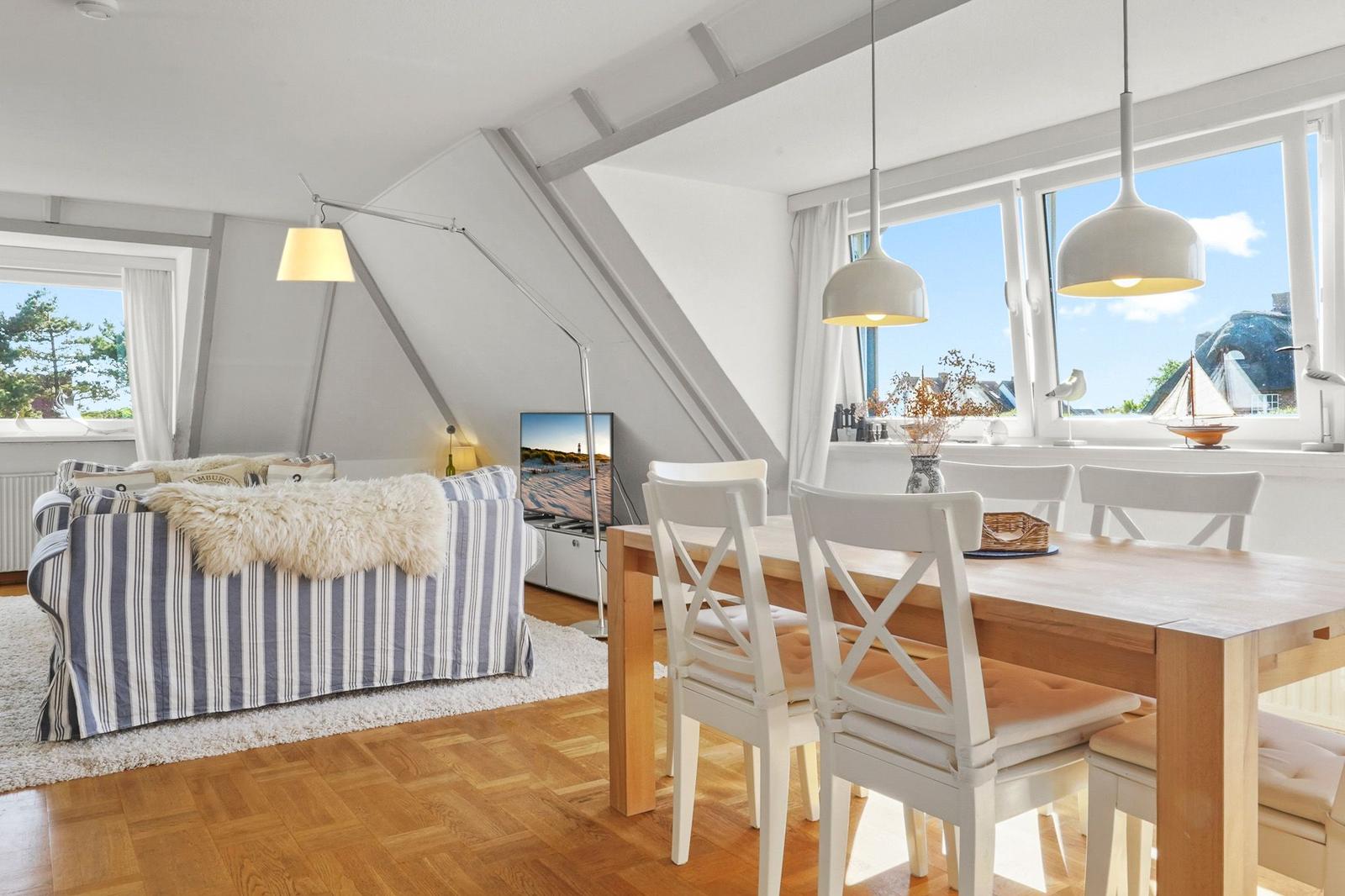 Wohn- und Essbereich mit Holzboden, Sofa, Tisch und Stühle. Große Fenster mit Blick.