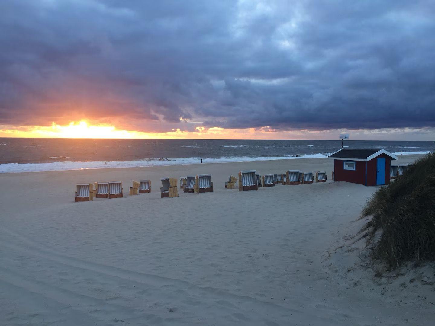Strand mit Strandkörben und rotem Strandhaus bei Sonnenuntergang.